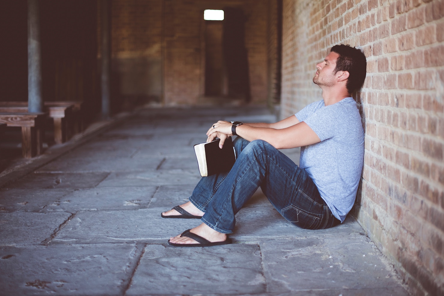 Man sitting against brick wall, book or bible in hand