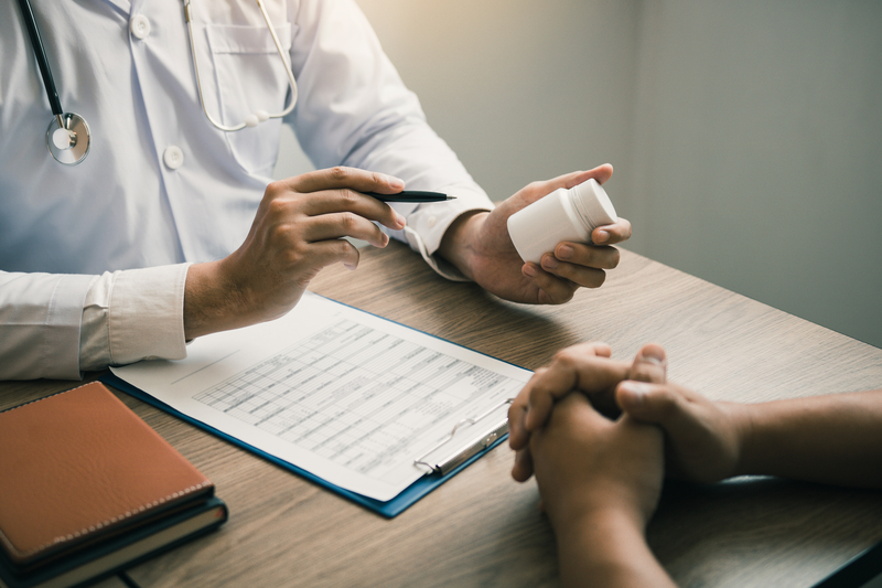 Doctor holds medicine container, explaining it to patient across the desk.