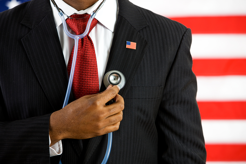 Man's chest and arm, hand holding stethoscope against chest, in front of American flag