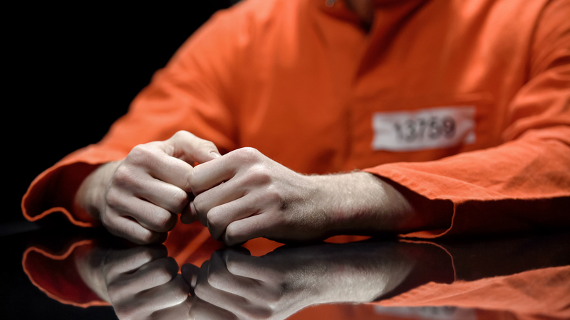 Prisoner sits at table, close up on hands.