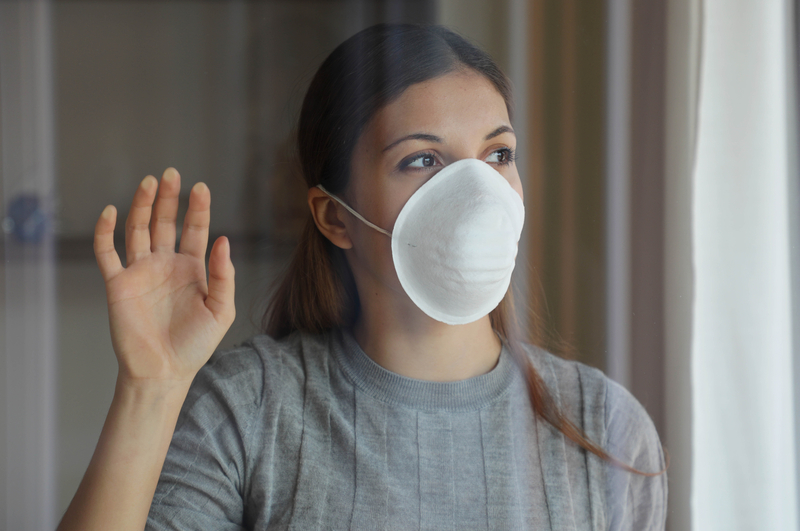 Woman in mask holds hand to window and looks out.