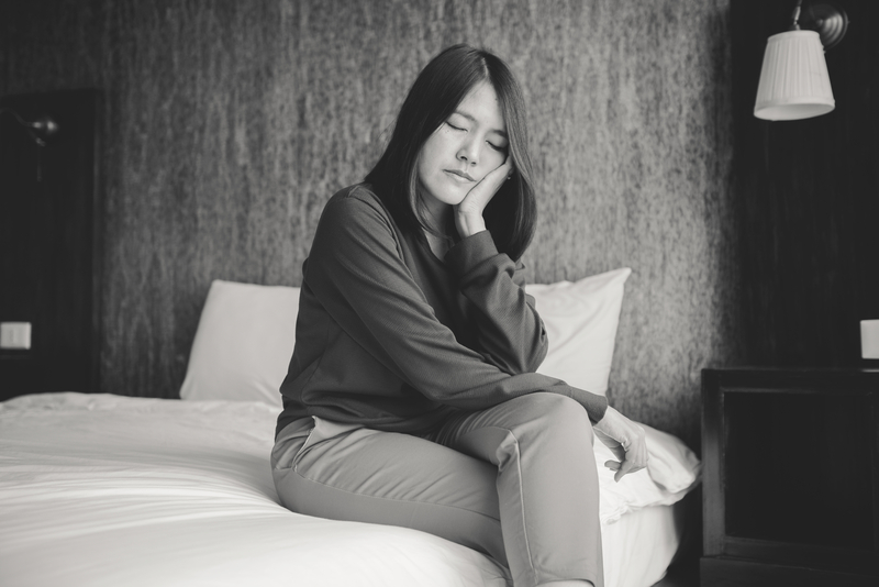 Black and white image of woman sitting on bed, appearing sad or depressed