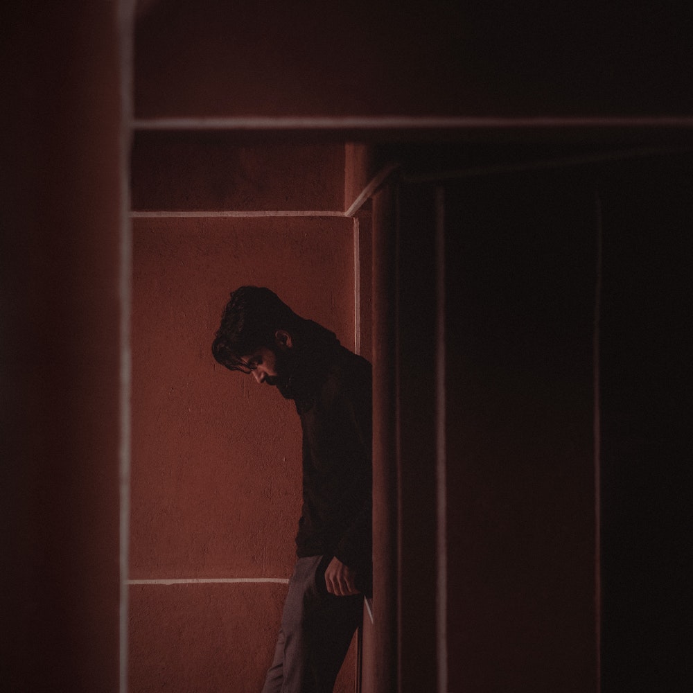 Man looking down, isolated, in a dark room.