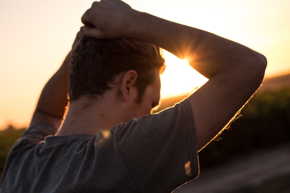 Man with hands on head, staring away, framed by sunset.