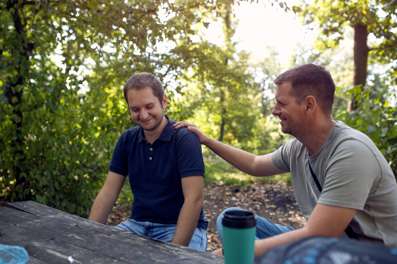 Two men outside in nature, one has hand on other's shoulder.