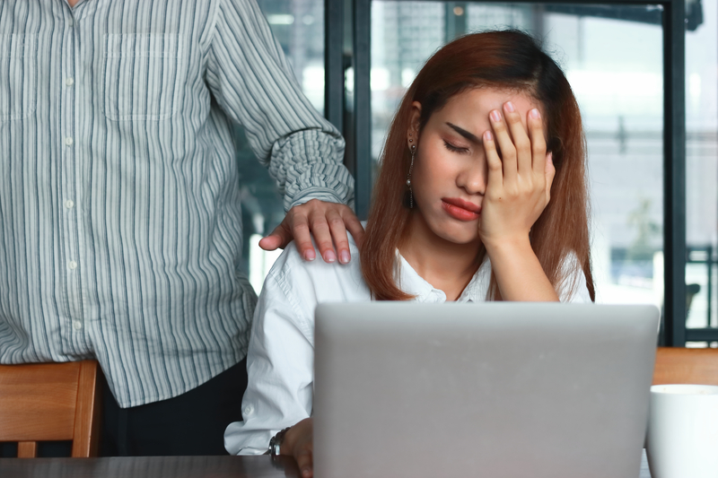 Distressed woman at computer, friend's comforting hand is on her shoulder.