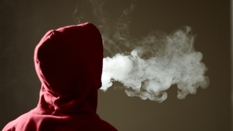 View of person in hoodie from the back, clouds of vape or cigarette smoke issuing from his head