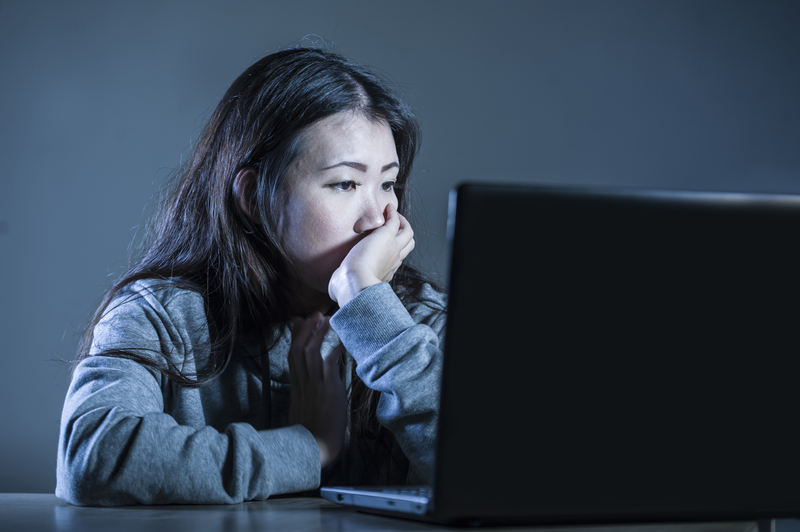 Woman sits looking at a computer screen, looks sad.