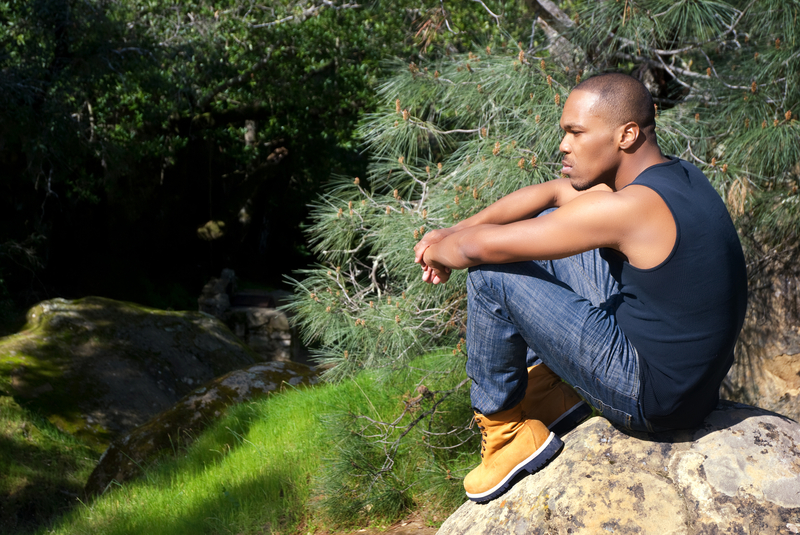Man sitting with hands on knees, contemplating, in nature