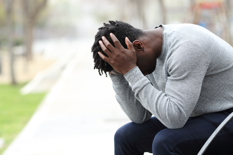 Black man sitting on a bench, head in hands, depressed or upset