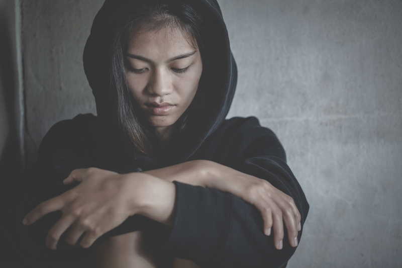 Depressed young woman sitting on ground, arms on knees, looking down