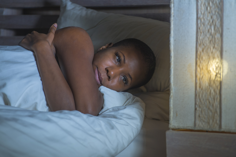 Sad or depressed African American woman lies on bed, hugs herself