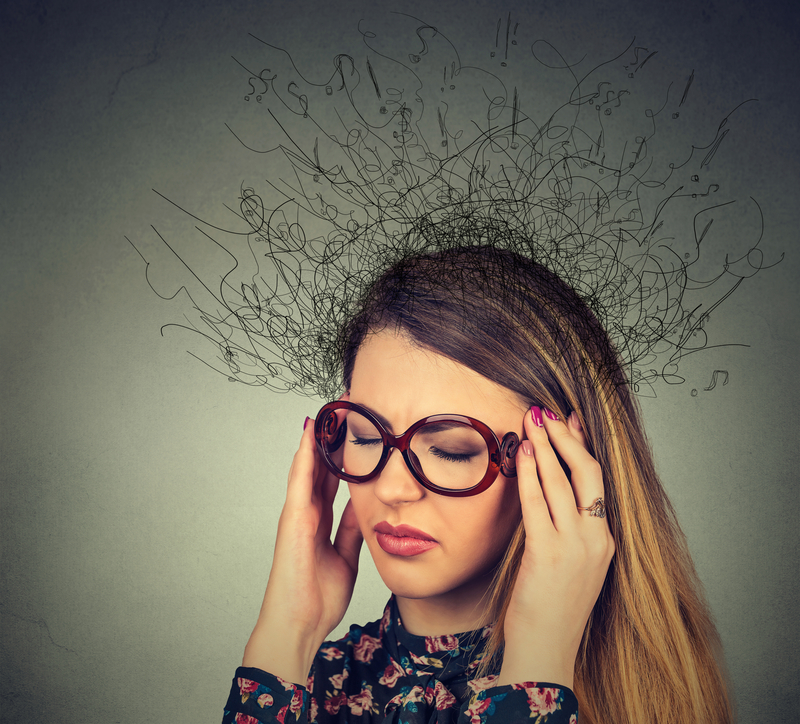 Woman with glasses and hands at temples. Drawn symbols and scribbles are coming out of her head.