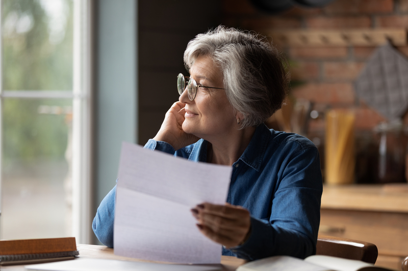 Woman holding piece of paper or letter sits at desks, looks to the side.