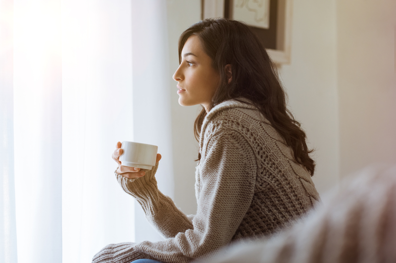 Woman with coffee mug looking out window.