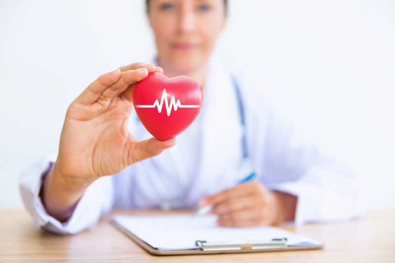 Doctor in blurry background holding plastic heart with ekg line in white on it